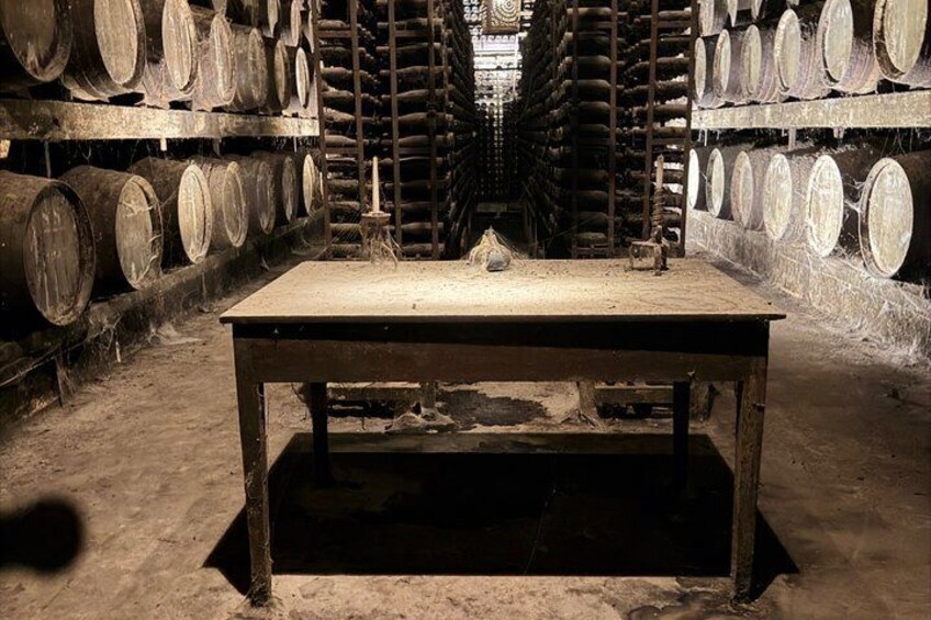 A wooden table in a cellar with barrels stacked in the background. 3