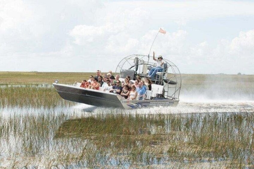 A boat with people on it, moving through a marshy area. 5