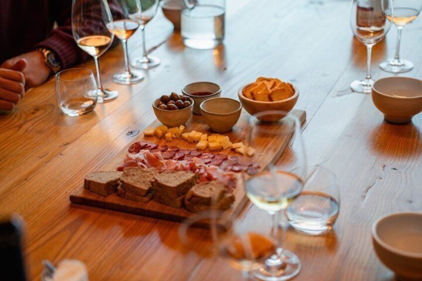 A wooden table with a charcuterie board, bowls of olives, cheese, and wine glasses. 5