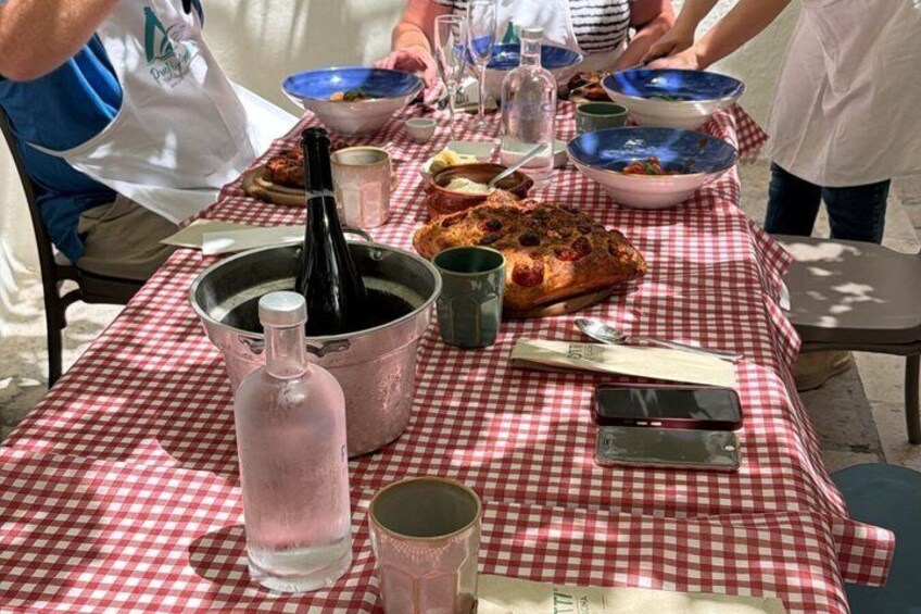 A picnic table with a checkered tablecloth, a bottle, a pan, a loaf of bread, and a pizza. 5