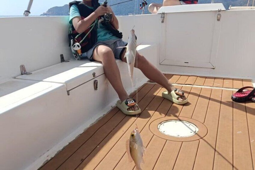 A person sitting on a boat deck with a camera, wearing a life jacket, and a backpack. 3