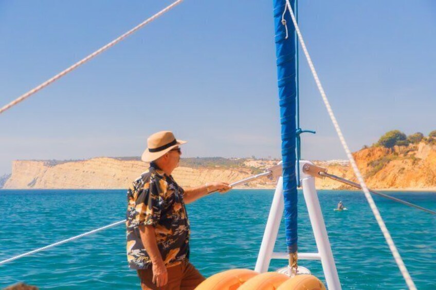 A person on a sailboat with a clear view of the sea and cliffs in the background. 2