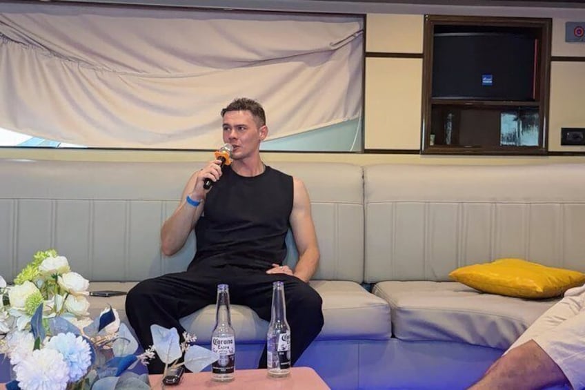 A person seated on a couch with a microphone, a bottle, and a glass on a table. 2