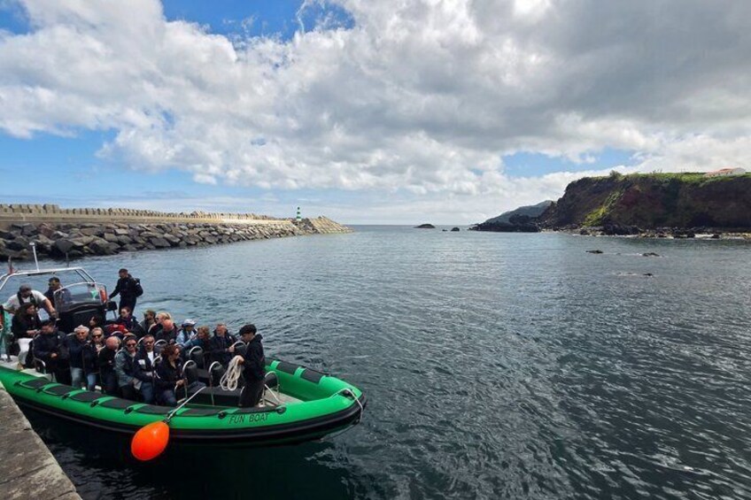 A green inflatable boat on calm water with a rocky coastline and a lighthouse in the distance. 1