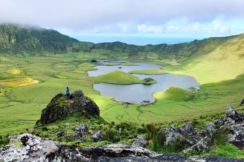 A person standing on a rocky outcrop overlooking a valley with multiple ponds and green fields. 5