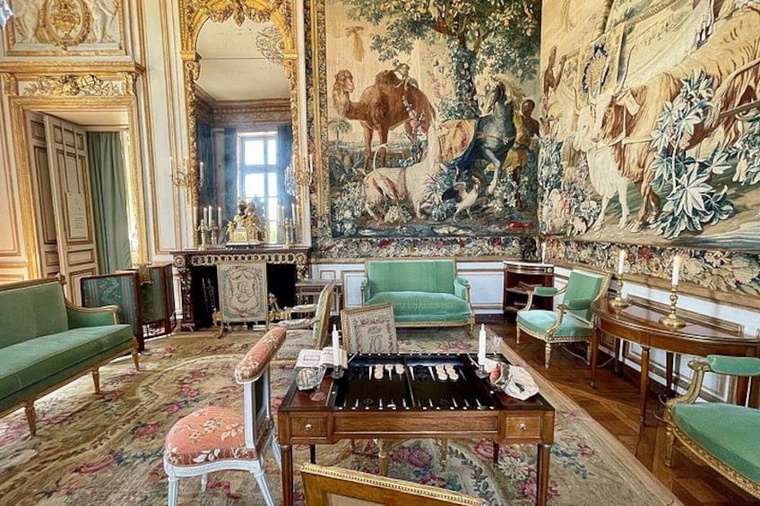 An opulent room with green upholstered furniture, a grand piano, and a large tapestry depicting historical scenes. 1