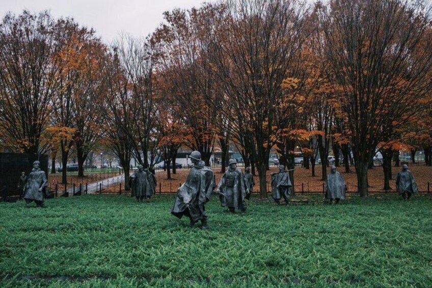 A park with statues of figures in raincoats, autumn trees, and a fence. 4