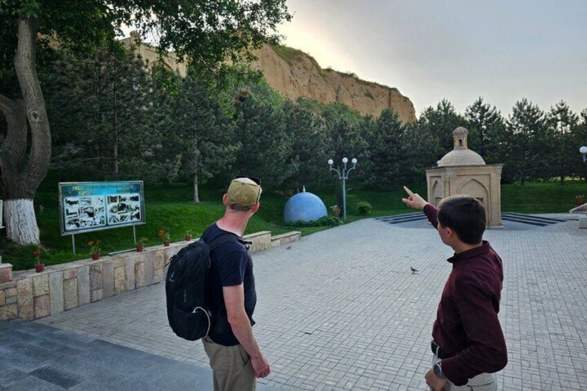 Two people walking on a paved path with a signboard and a small dome structure in the background. 4