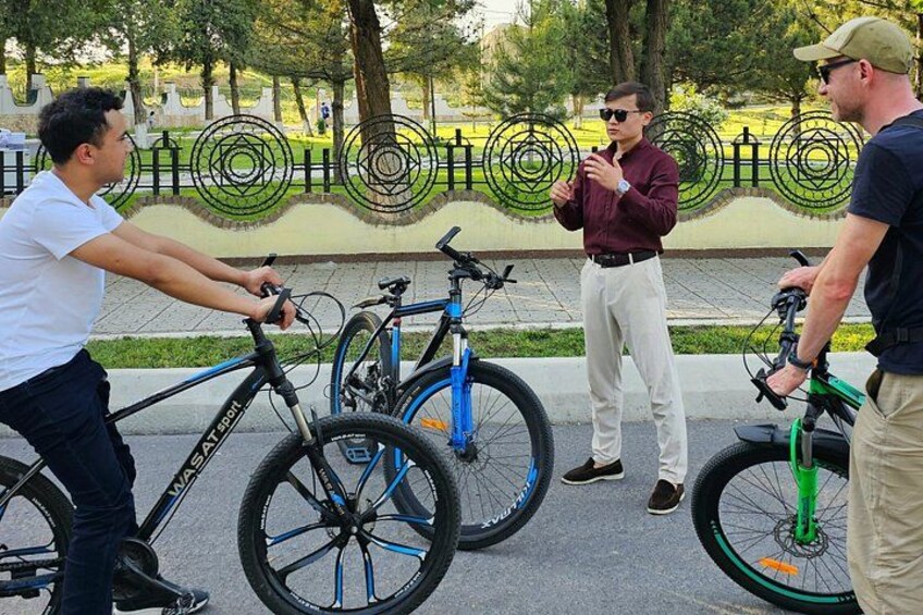 Three people interacting with bicycles in a park. 4