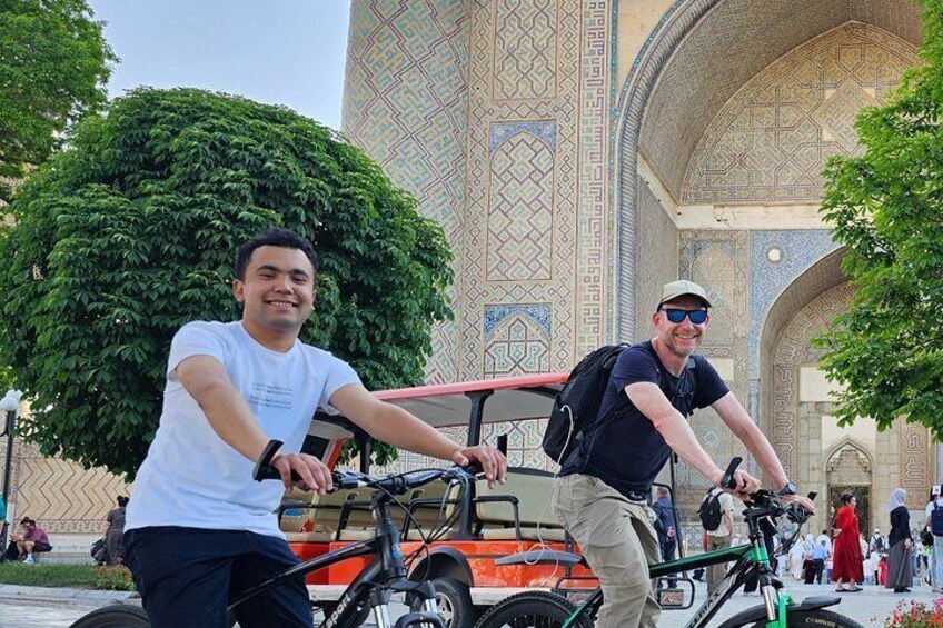 Two people riding bicycles in front of a large, ornate building with intricate tile work. 3