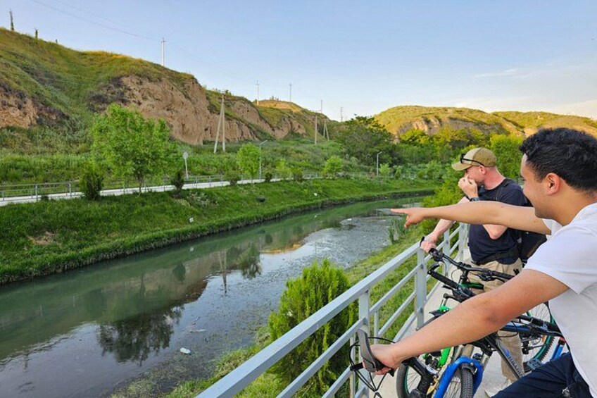 A river with a bridge, greenery, and hills. 5