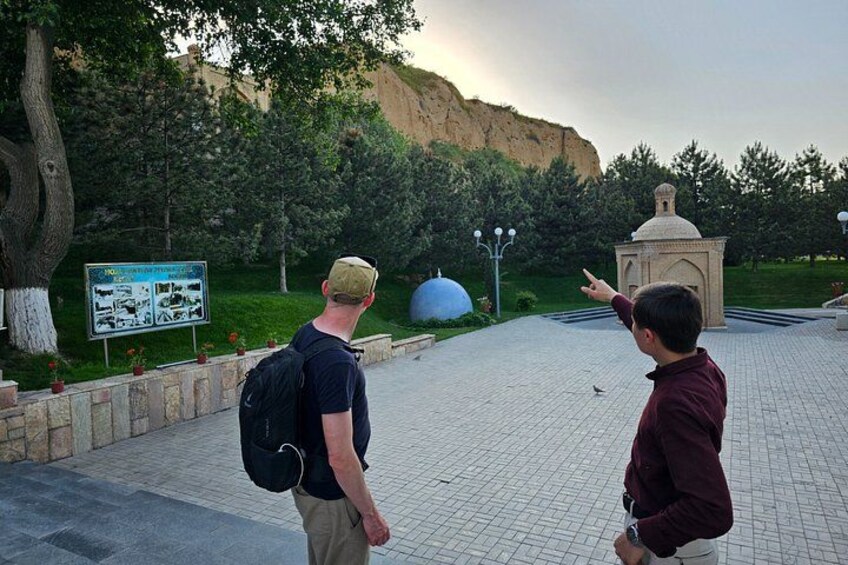 Two people walking on a paved path, a signboard, a small building, and a large blue dome in a park. 2
