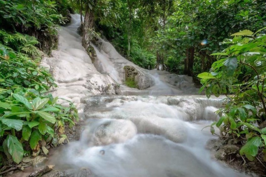 A waterfall in a forested area with rocks and greenery. 2