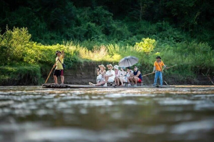 People on a riverbank, some standing and others sitting, with a guide leading a boat. 2