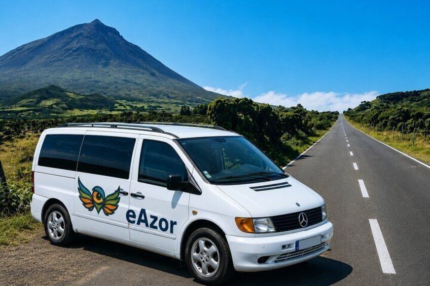 A white van with 'eAzor' and a bird logo parked on a road with a mountain in the background. 1