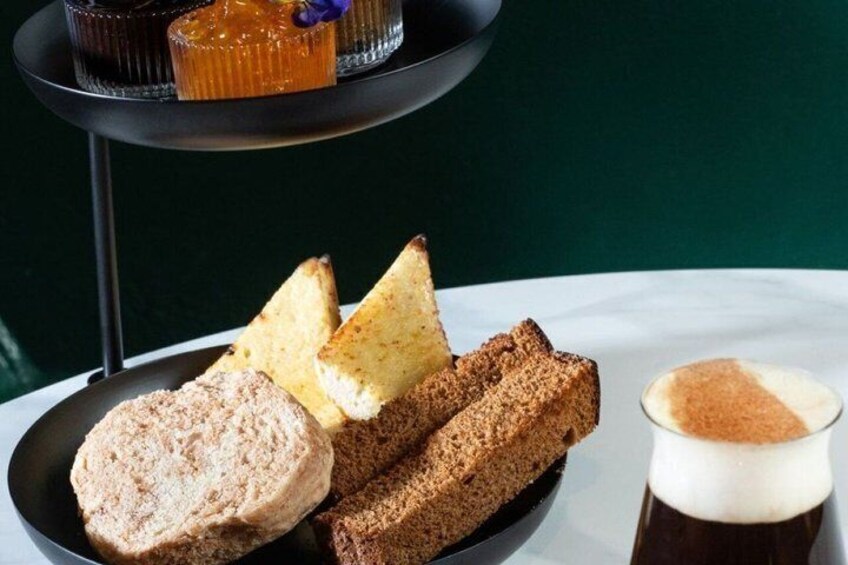 A plate with bread, a glass of coffee, and a dessert on a table. 3