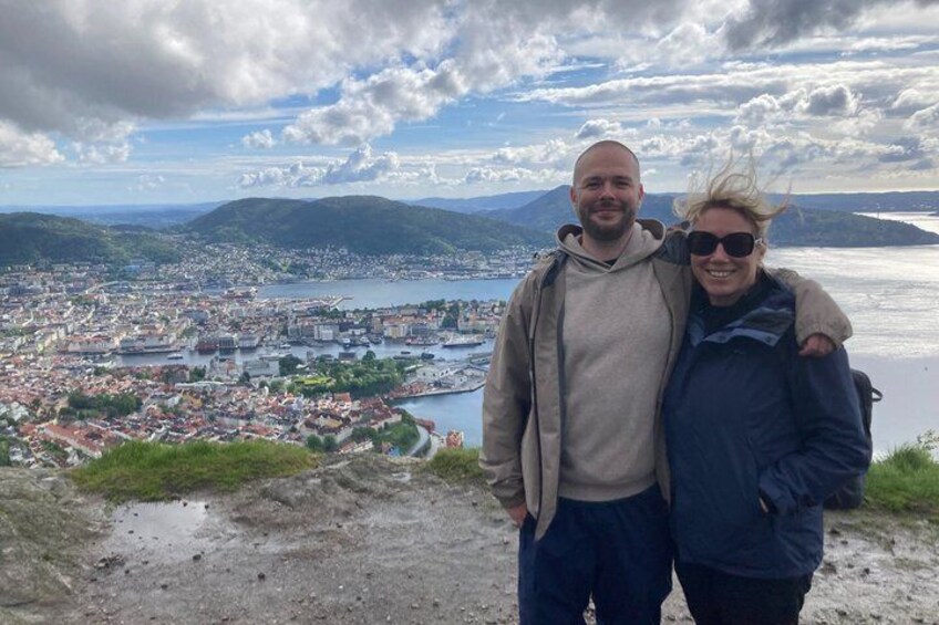 A couple standing on a hill overlooking a city with a river and mountains in the background. 3