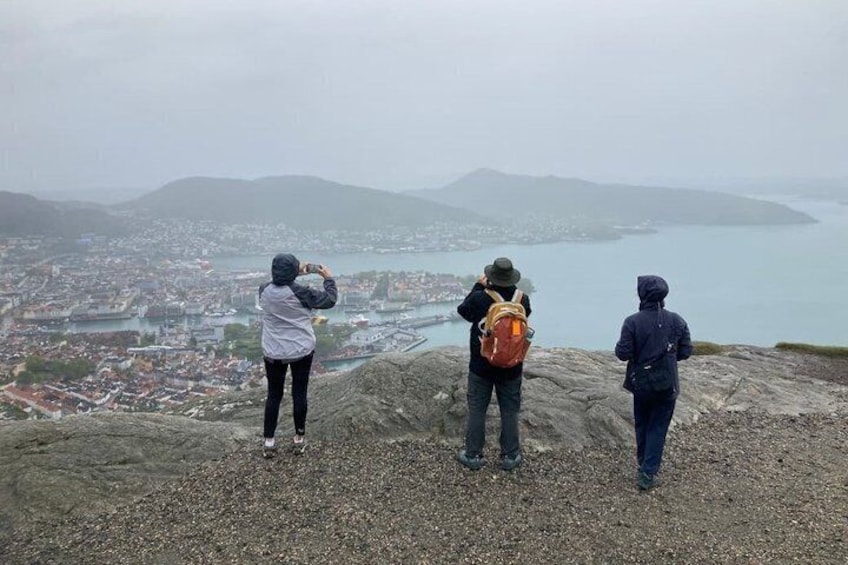Three people standing on a rocky outcrop overlooking a city and a body of water. 5