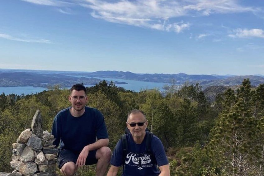 Two people sitting on a stone structure with a scenic view of hills and a body of water in the background. 4