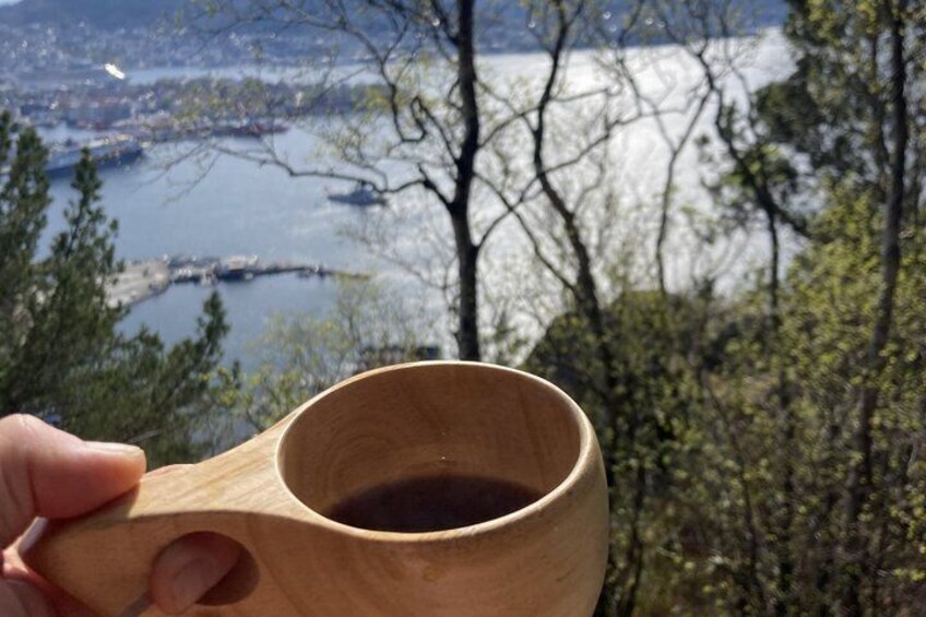 A hand holding a wooden cup with a view of a lake and trees in the background. 1