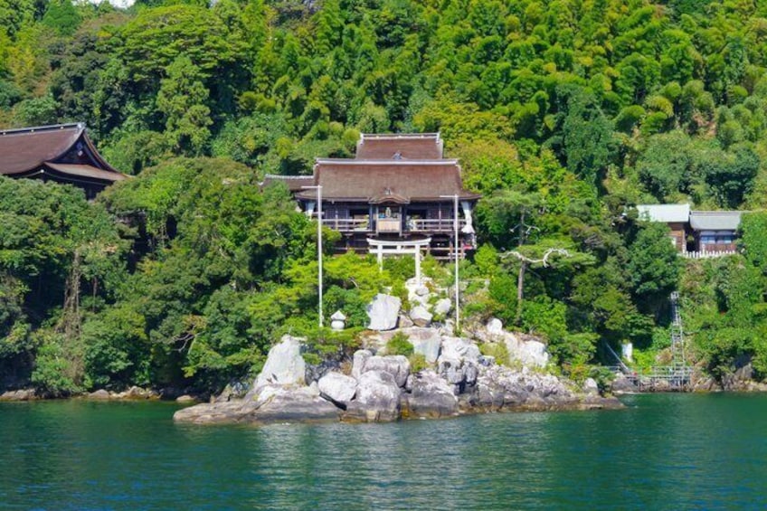 A traditional Japanese building on a rocky island surrounded by water and dense forest. 1