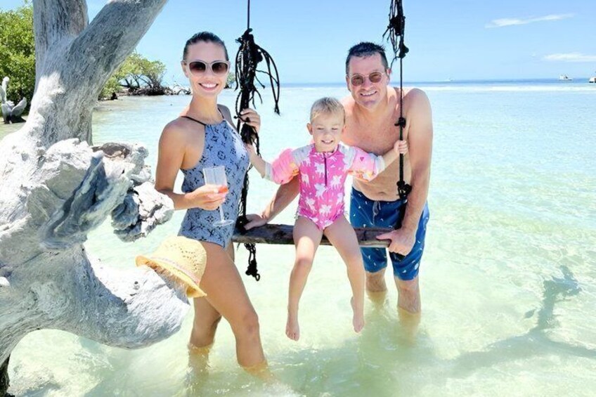 A family on a beach swing with clear water and a tree. 2