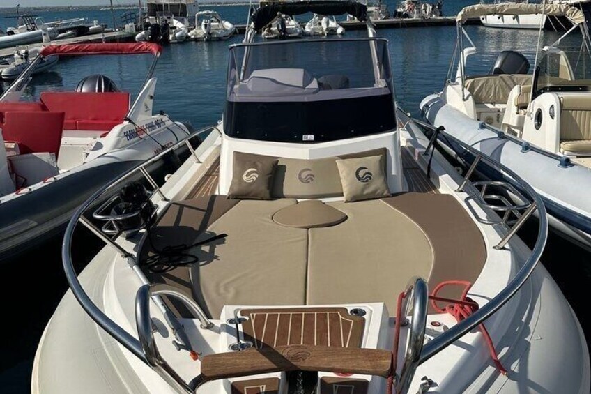 A boat's deck with a cushioned seating area, a steering wheel, and a wooden floor. 1