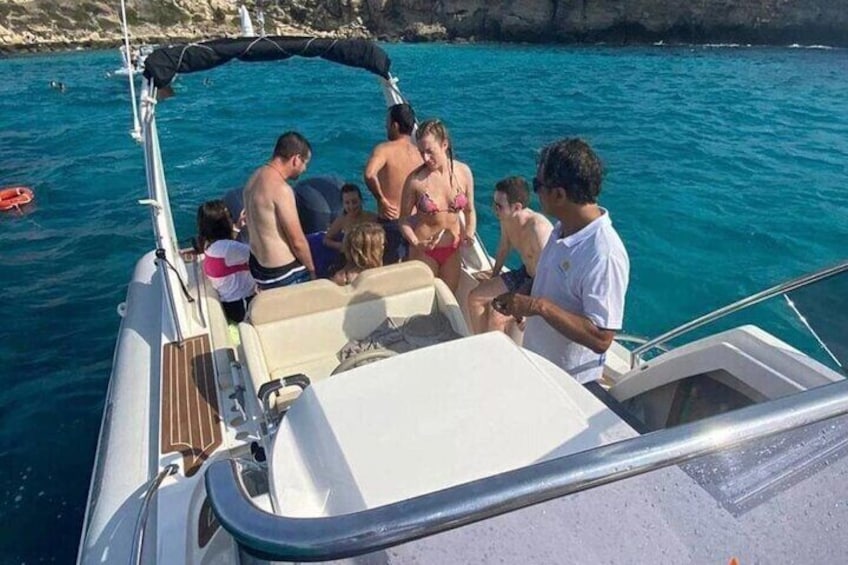 A group of people on a boat with clear blue water and rocky cliffs in the background. 1