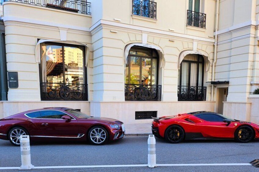 Two red sports cars parked on a city street in front of a building with large windows and balconies. 4