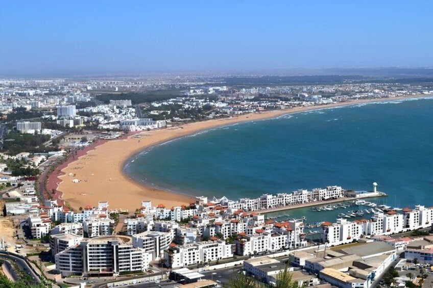 A coastal cityscape with a curved beach, a marina, and residential buildings. 1