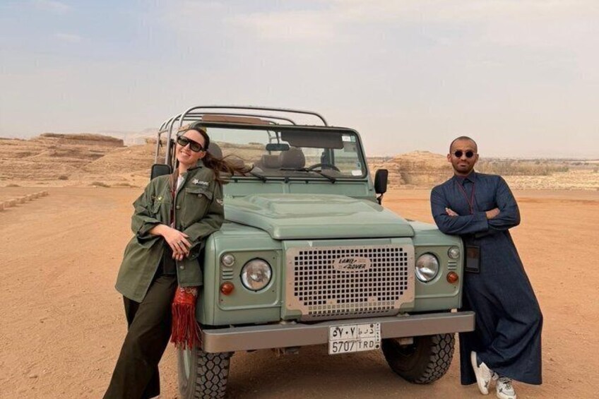A desert landscape with a green off-road vehicle parked in the foreground. 1