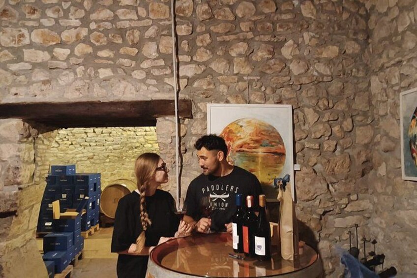 A person standing at a counter with wine bottles, a stone wall, and a painting of a planet in the background. 1