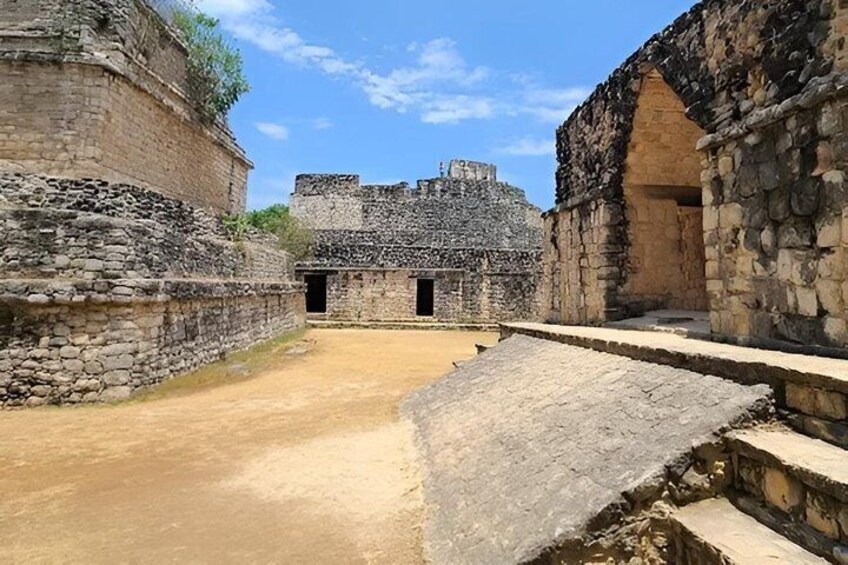 An ancient stone structure with a central courtyard and a large building in the background. 2