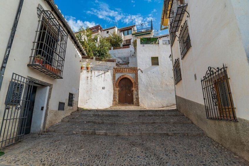 A cobblestone street leading to a building with a wooden door and a small archway. 3