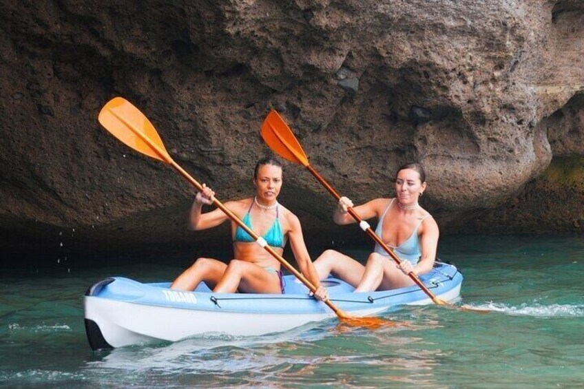 Two people kayaking in a blue raft with orange paddles, surrounded by rocky cliffs. 3