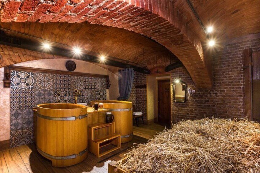 A rustic cellar with wooden barrels, a tiled wall, and a straw-covered floor. 3