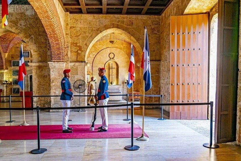 A historical building with stone arches, a red carpet, and flags. 1