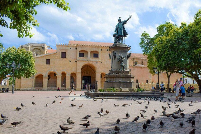 A plaza with a statue, pigeons, and historic buildings. 5