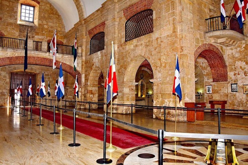 A historic building with stone walls, arched doorways, and flags. 4