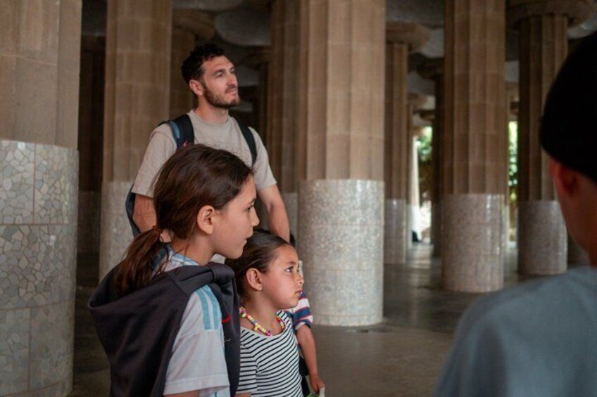 A corridor with columns, a person carrying a child, and another person standing in the background. 5