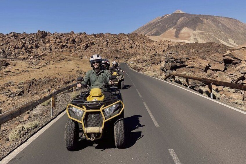 A group of people on ATVs on a paved road with rocky terrain and a mountain in the background. 3