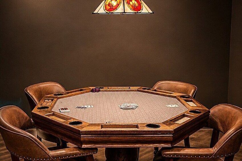 A wooden oval poker table with cards and chips, surrounded by leather chairs. 3