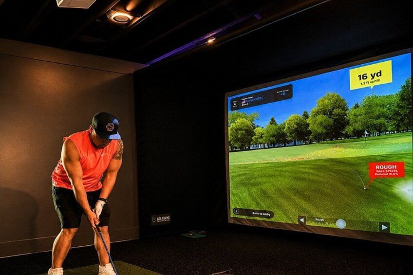 A person playing golf indoors with a large screen displaying a golf course. 3