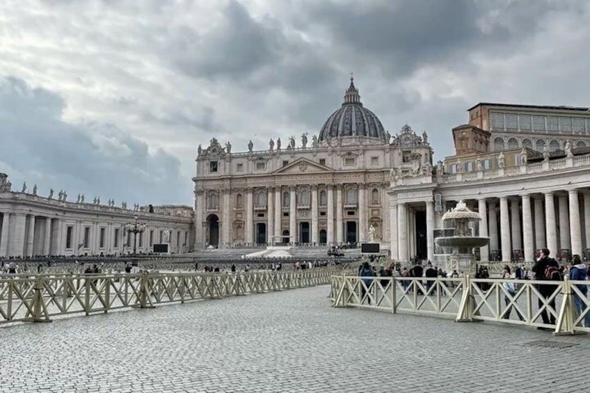 St. Peter's Basilica with a large dome, a fountain, and a crowd of people in front. 1