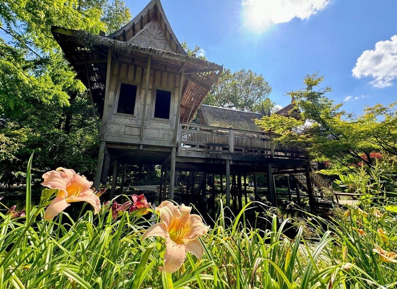 A traditional wooden house with a thatched roof, surrounded by lush greenery and flowering plants. 3