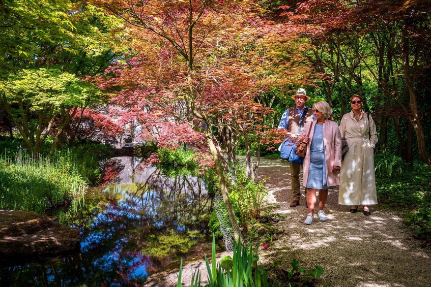 A group of people walking on a path through a park with a pond and trees with autumn foliage. 4