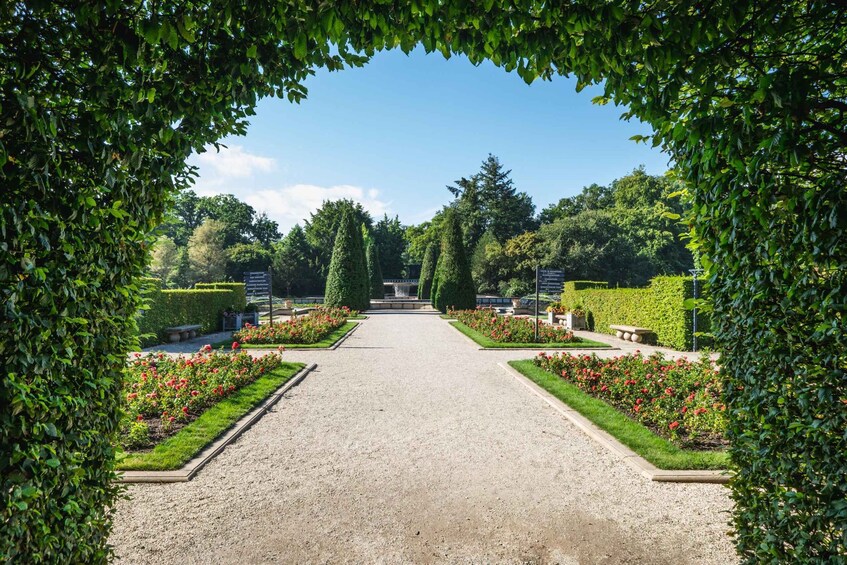A formal garden with a gravel path, neatly trimmed hedges, and red flowers. 1