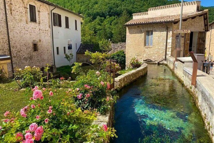 A narrow water channel, stone buildings, and blooming pink flowers. 4