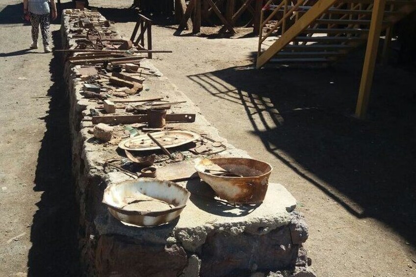 A row of old, rusted metal objects and tools, possibly from a historical site or workshop, with a person walking in the background. 3