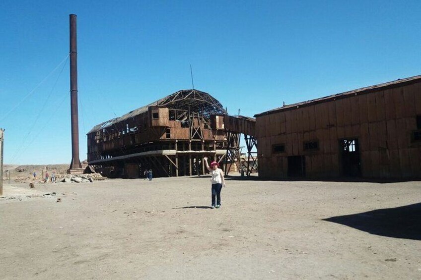 A large, rusted industrial building with scaffolding, a tall chimney, and a clear blue sky. 2